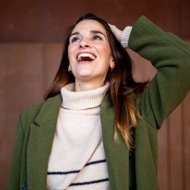 A woman in a green coat laughing with her head tipped back