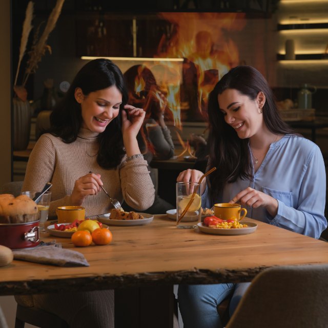 Two friends eating and laughing together beside a fire
