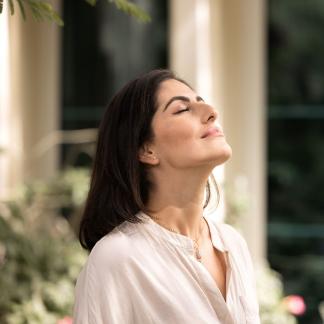 A woman with her eyes closed, face tipped up to the light